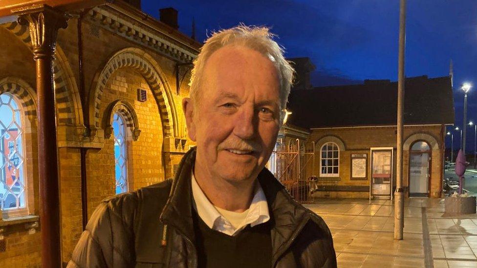 Man with short grey hair at a railway station