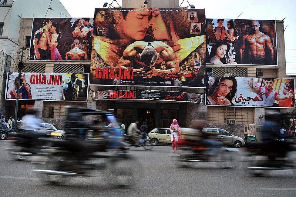 In this photograph taken on January 14, 2009 commuters pass a cinema displaying billboads advertising the Indian Bollywood film 'Ghajini' in Karachi. Just a year ago, the screening would not have been possible, as Pakistan had barred films from its rival neighbour for more than 40 years. Lifting the ban has helped revive Pakistan's suffering cinemas, luring film buffs away from the flat-screen televisions in their living rooms and into the movie houses.