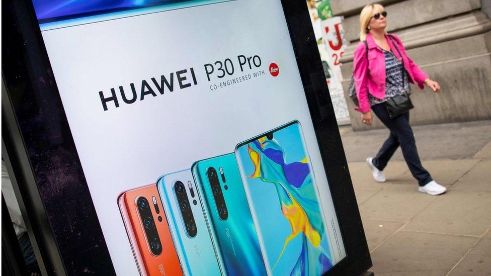 Woman walks past Huawei advert on bus stop