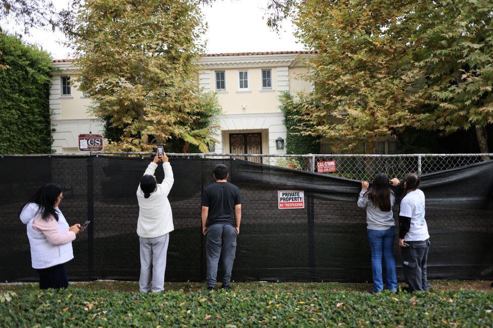 People peering over a fence to take a look at the house where the murders happened.