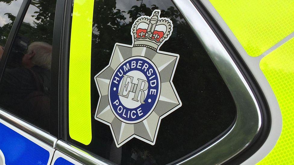 A close-up of the back window of a Humberside Police patrol car, with the force's badge on the glass.