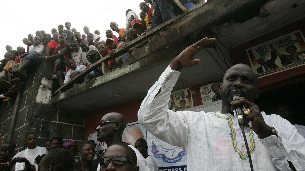 Liberian footballer George Weah (R) as he campaigns for Liberia's 2005 presidential elections in Monrovia watched by people sitting on a roof