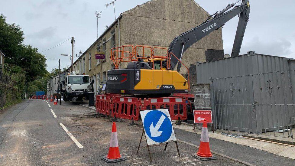 Demolition work on homes in Cyfyng Road, with a digger close to houses and cones and an arrow sign in the street