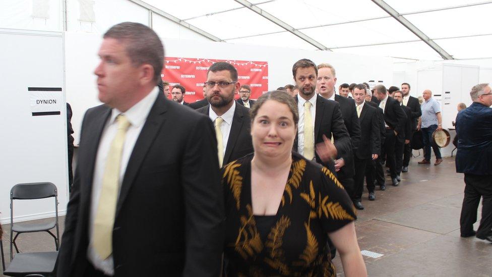 Cor yn cerdded tuag at y llwyfan // A choir walking towards the stage