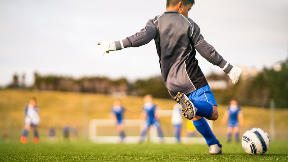 A child wearing a blue and black strip goes to take a kick while other players stand in the background.