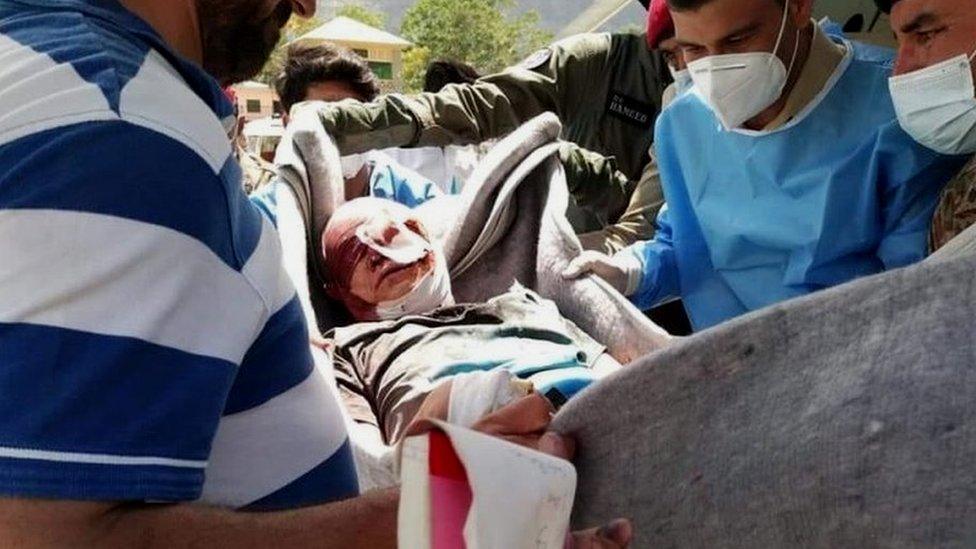 Handout photo shows Pakistani rescue officials shifting an injured person to hospital after a blast at a bus carrying Chinese engineers to the site of Dasu Dam in Kohistan, Pakistan, 14 July 2021.