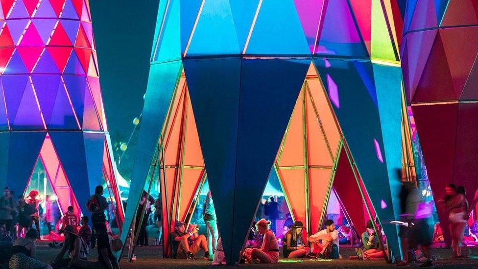 Sarbalé Ke structures with hollow interior and colourful patterns on them. There are people sitting inside the hollow interior.