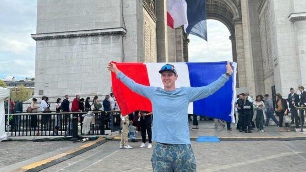 Lucca Froud holding a Parisian flag standing in front of the Arc de Triomphe in Paris