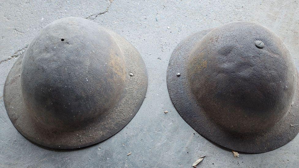 Two World War One helmets repurposed for use in World War Two. They are lying rim down on the ground and are rusty.