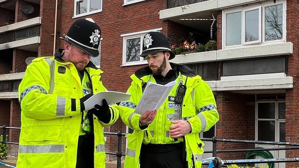 Two police officers outside flats at Carlton Way, Cambridge