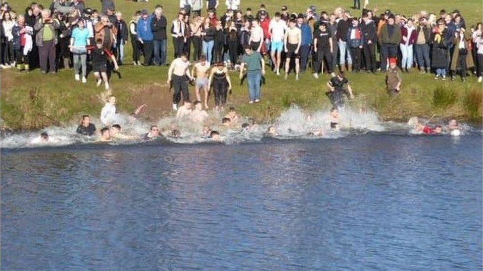 Lots of players diving into the river Aln at the end of the Shrovetide Football game with dozens of people watching