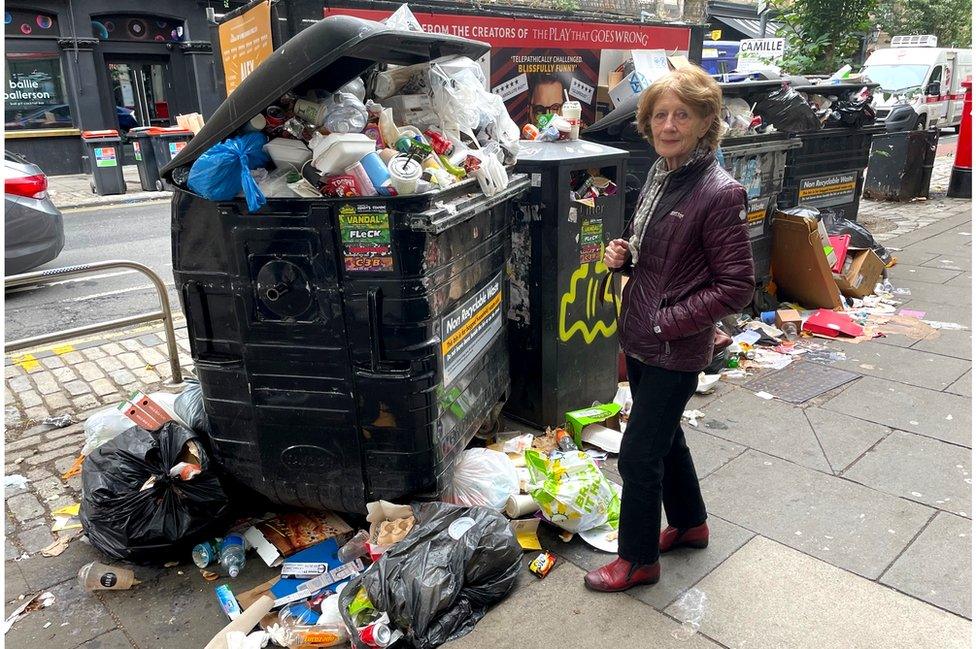 Anne Starsmeare beside a pile of rubbish that is taller than her