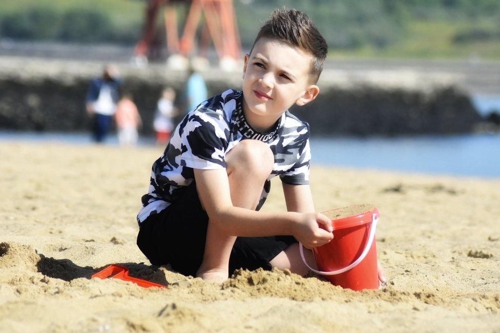 A young boy fills a plastic bucket with sand on the beach