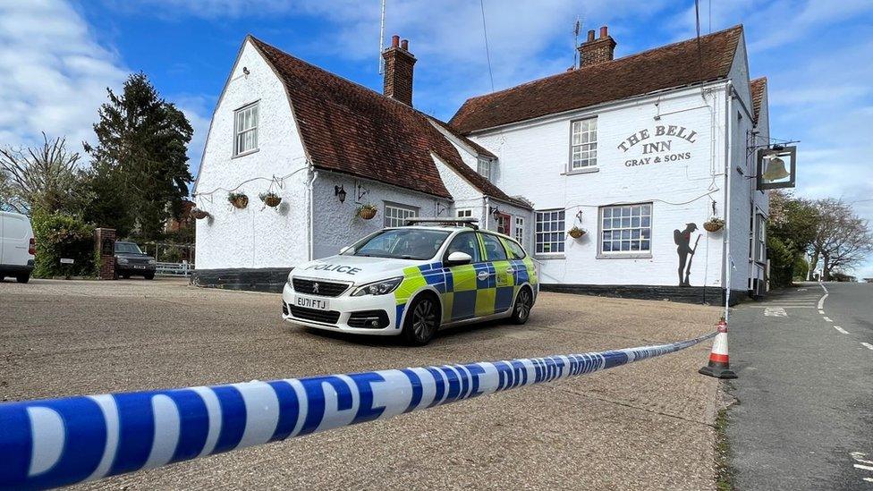 A pub in Colchester. The building is white and has The Bell Inn Gray & Sons written on it. A Essex Police car is parked at the pub and a police cordon has been put in place