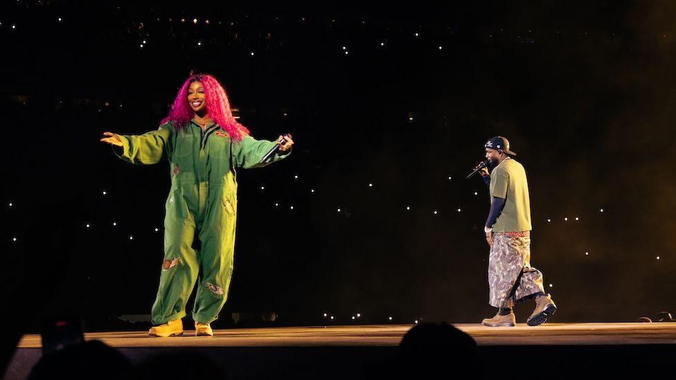 SZA appears in a jumpsuit alongside Kendrick Lamar in a green top and trousers