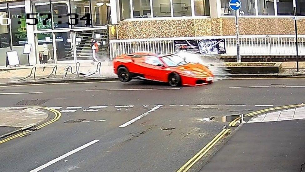 Red Ferrari bouncing off a kerb with its back wheels in the air after hitting a barrier in Norwich city centre.