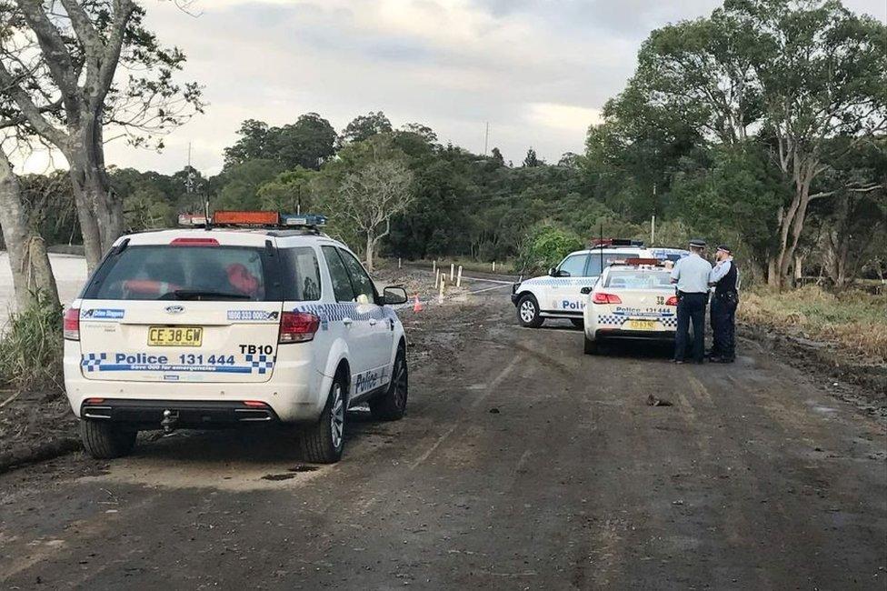 Police guard the site where a car left the road and entered the Tweed River.