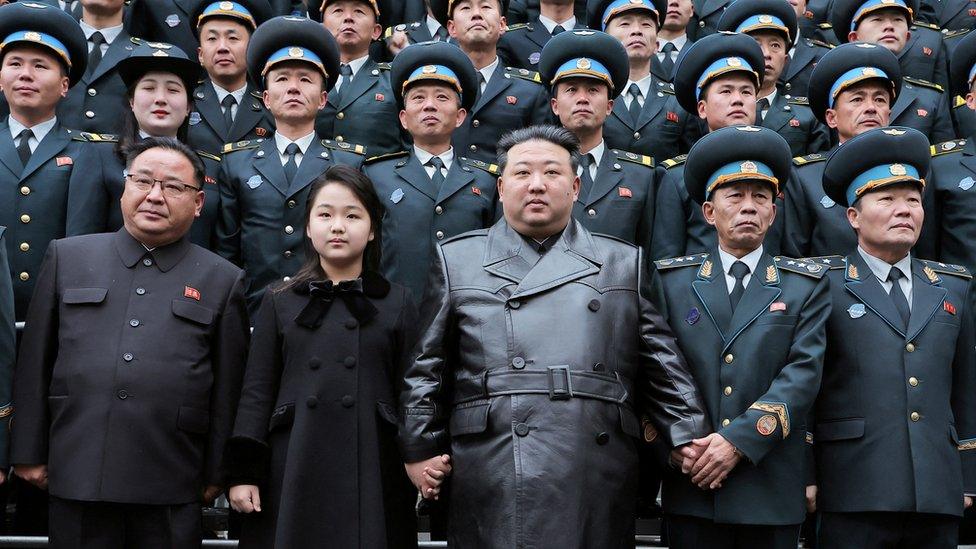 Kim Jong Un,clasping hands with his daughter (left), poses for a picture with scientists and engineers who worked on the North's satellite launch.