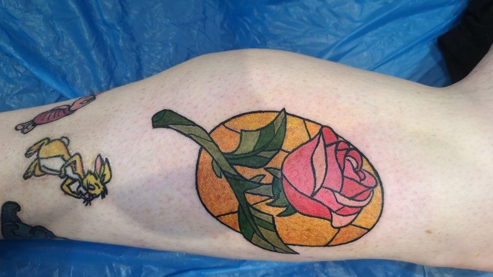 A leg with a tattoo of a rose and Disney characters