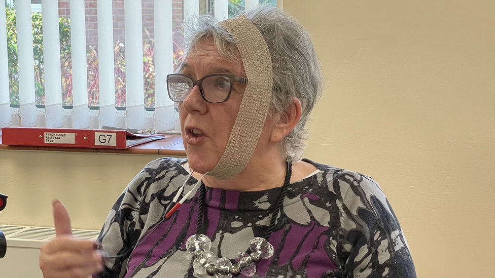 Jane Davenport with band around her head, under her chin, while using neuro-muscular stimulation