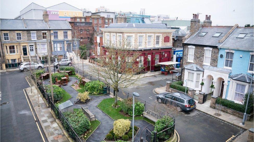 An aerial image showing the set of Albert Square in EastEnders. There is a small central garden surrounded by black railings, and the Queen Victoria pub is straight opposite. Notable character's homes surround the square.