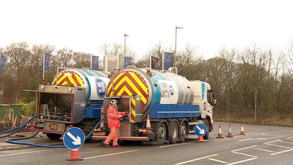 Two water tankers parked side by side a person in high-vis stands at the back of one.