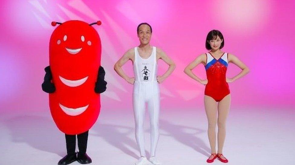 Hideo Higashikokubaru stars with a gymnast (R) and an alien sausage mascot (L)