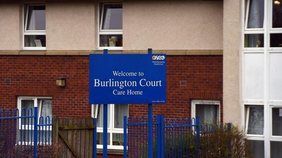 Outside a brown brick building with a blue sign that reads 'Welcome to Burlington Court Care Home'.