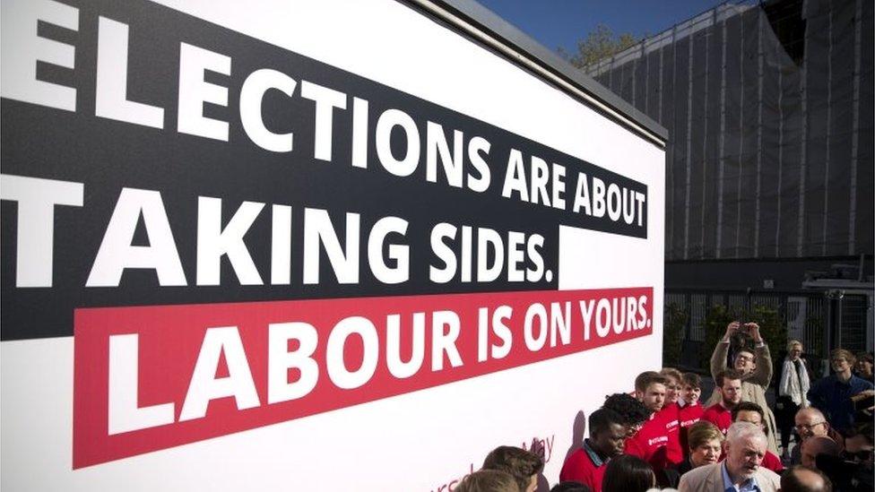 Jeremy Corbyn campaigning with Labour supporters in front of billboard saying: Elections are about taking sides. Labour is on yours.