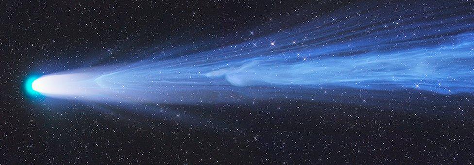 Comet moving from right to left, with long blue wind-like tail coming from the end.