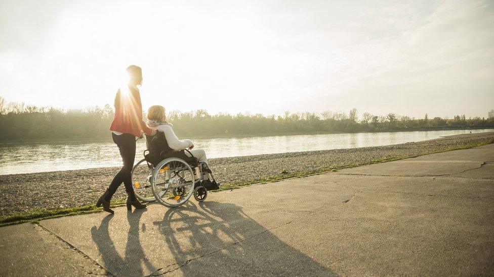 A woman pushing another in a wheelchair