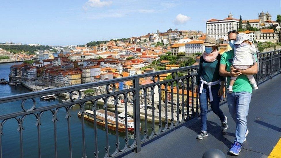 A couple wearing masks walk with their child across the Dom Luis I Bridge in Porto, Portugal