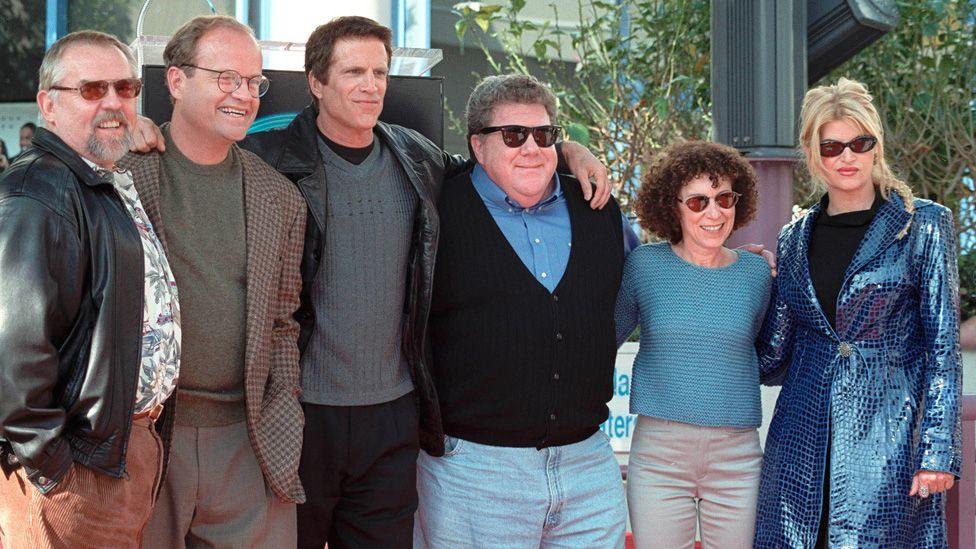 Cheers co-stars standing in a row with with their arms around each other in 1999. Left-right: John Ratzenberger, Kelsey Grammer, Ted Danson, George Wendt, Rhea Perlman and Kirstie Alley.
