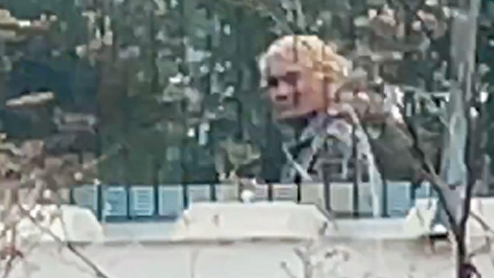 A zoomed in image taken from our undercover filming of a Vietnamese people smuggler, hair dyed blonde, walking behind a fence