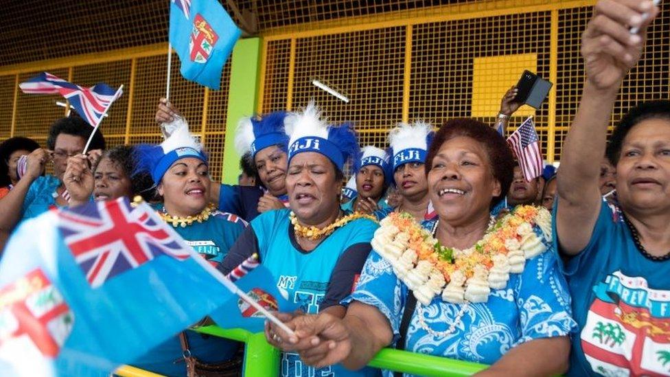 People wave flags as Meghan, Duchess of Sussex, visits an indoor market in Suva, Fiji October 24, 2018