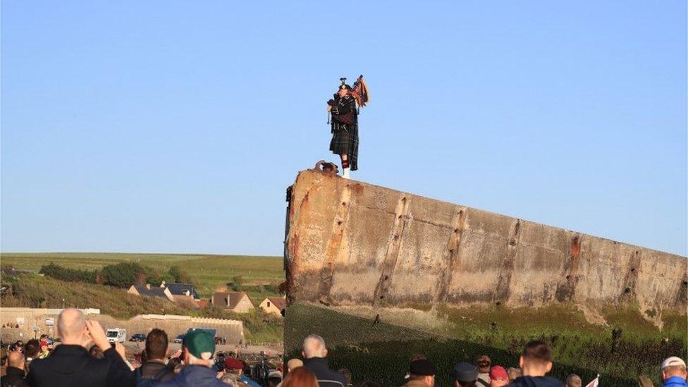 A lone piper plays on the Mulberry harbour at Arromanches in Normandy