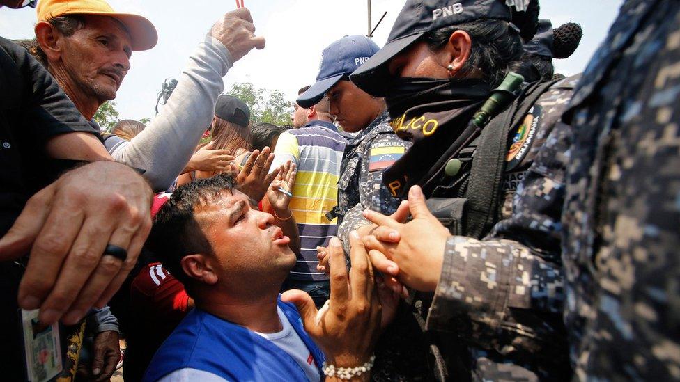 A supporter kneels in front of Bolivar state security forces