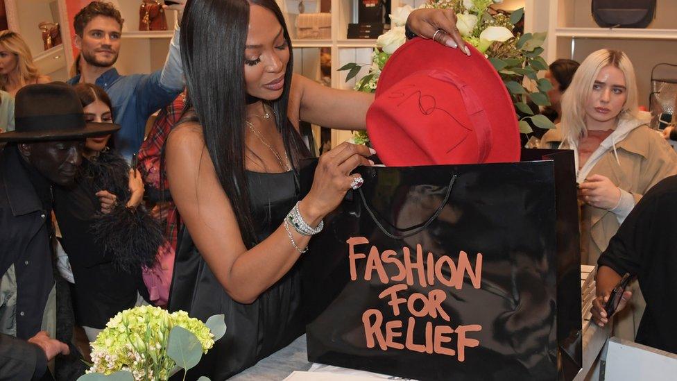 Naomi Campbell putting a red hat into a Fashion for Relief bag