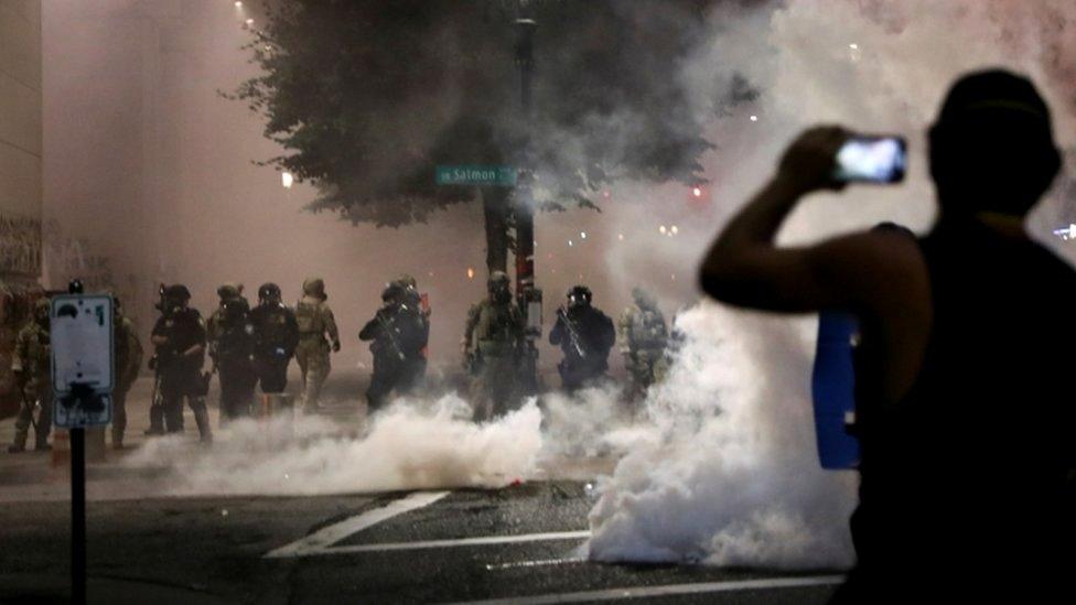 A demonstrator holds a mobile phone in front of federal law enforcement officials during a protest in Portland, Oregon