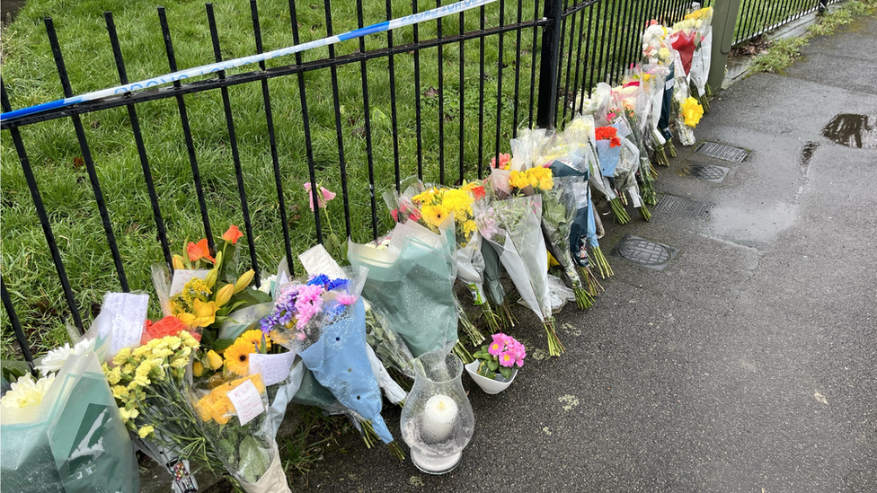 Flowers up against a fence with police tape on it