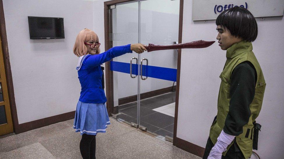 Young woman in a blue uniform points a cartoon style sword at the face of a young man in a green outfit