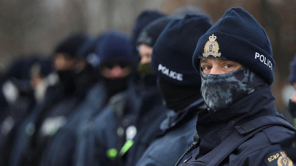 Police in a line-up stretch as far as the frame - with one turning to look directly into the camera