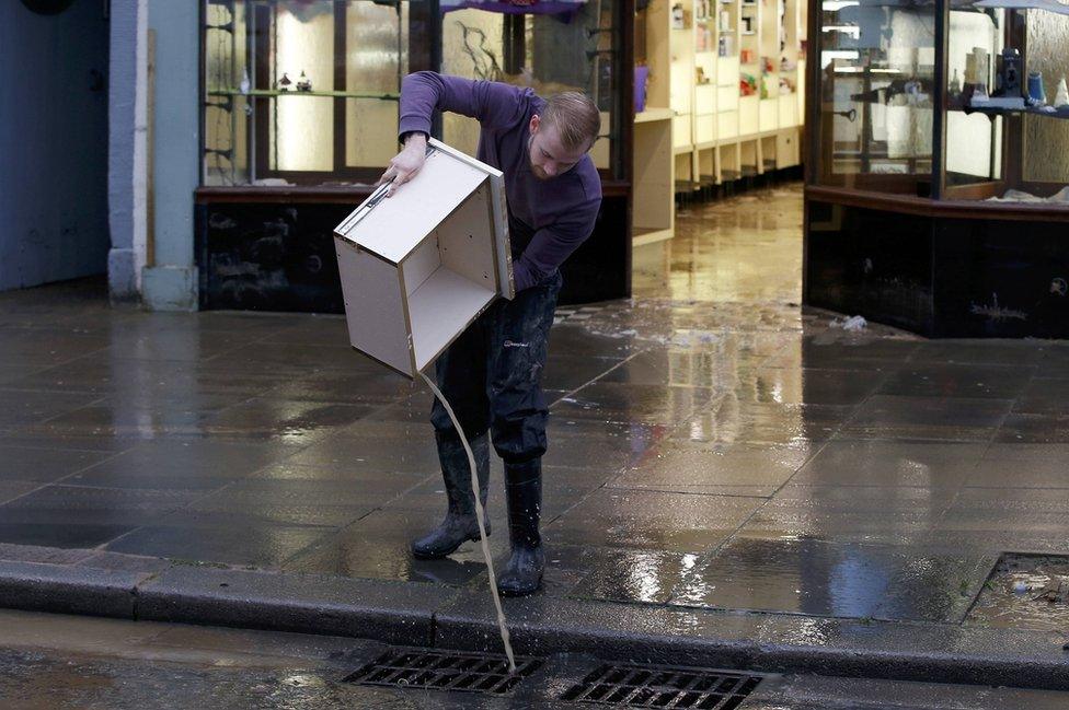 A man cleans floodwater from a business in in Cockermouth