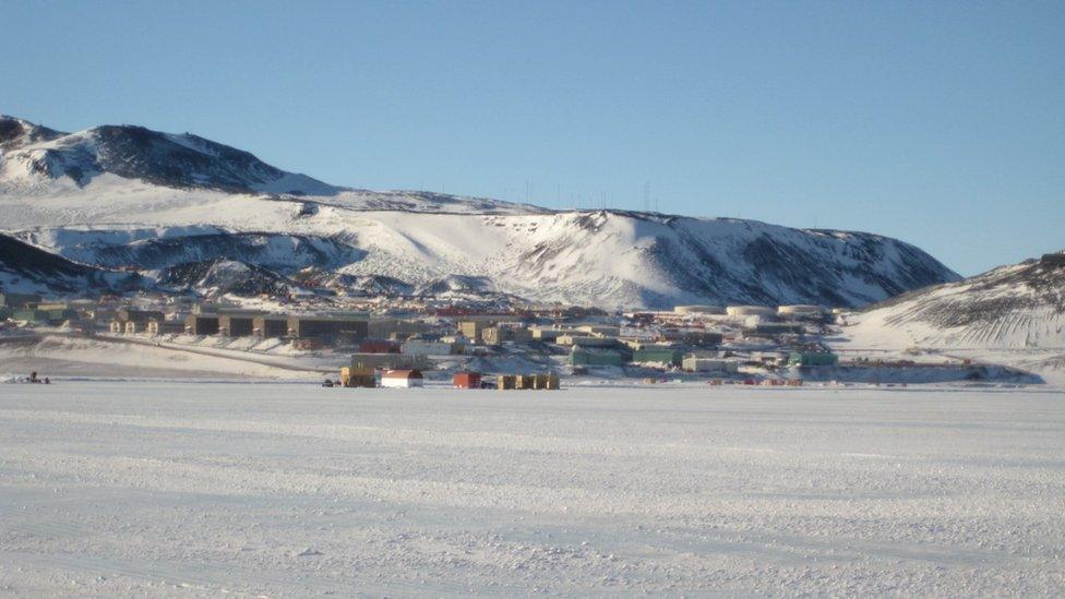 A collection of buildings at the base of a slope, dusted in snow