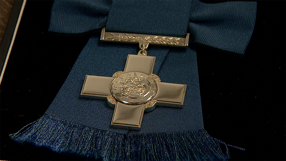 A close-up of a George Cross medal on a blue ribbon and lying in a black case