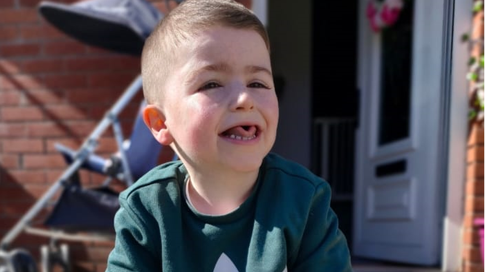 Kai Reynolds, nine, smiles while sitting in his back garden wearing a green tracksuit