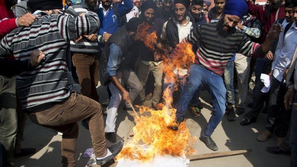 Kashmiri Sikhs kick a burning effigy of Gurmeet Ram Rahim Singh, chief of a religious sect Dera Sacha Sauda, during a protest against the killing of two Sikh boys, in Srinagar, Indian controlled Kashmir, Saturday, Oct. 17, 2015