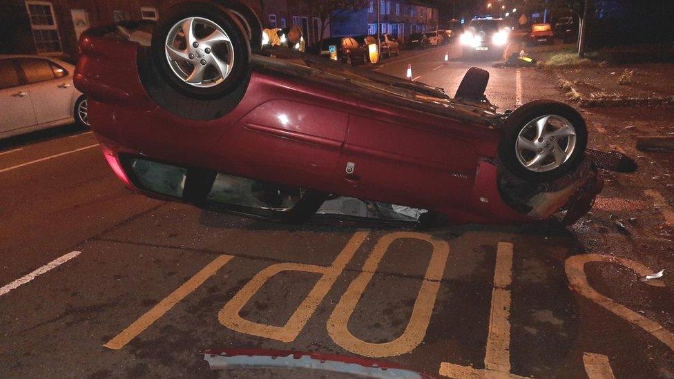 Red car with its wheels in the air just beyond the "stop" of a bus stop sign painted on the road