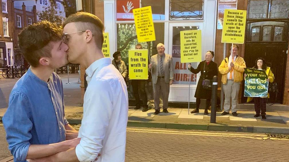 Joe Fergus and Robert Brookes kissing in front of protesters