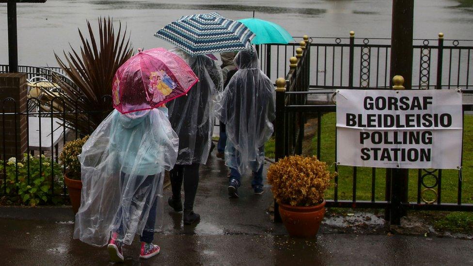 people with umbrellas entering polling station